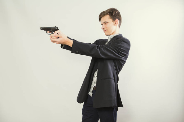 gunman ready to shoot, light background. Portrait shot of a man in a suit aiming with a gun. Copy space - Foto, Bild