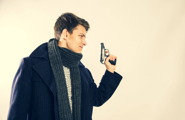 Front view of a young cop in a coat and scarf holding a gun in his left hand - Foto, Imagem