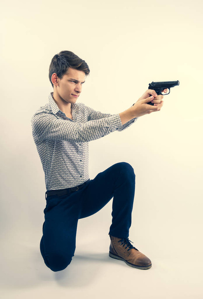 mężczyzna w biznesie ubrania siedzi na kolanie i strzelanie z pistoletu izolowane na jasnym tle - Zdjęcie, obraz