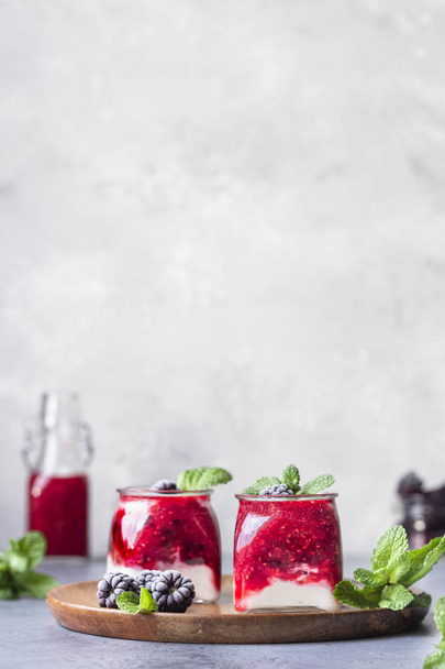 Glass jars of healthy layered berries and yogurt smoothie. Mix berry smoothie with raspberry, blackberry and yogurt. Wellbeing and weight loss concept. Selective focus, toned image. - Photo, Image