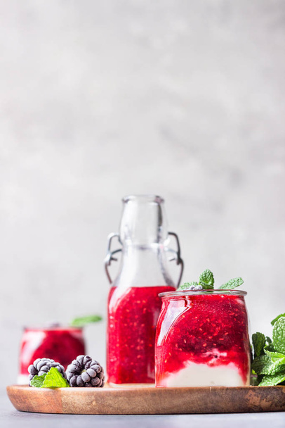 Glass jars of healthy layered berries and yogurt smoothie. Mix berry smoothie with raspberry, blackberry and yogurt. Wellbeing and weight loss concept. Selective focus, toned image. - Zdjęcie, obraz