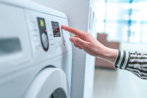 Housewife using display and button for turning on and choosing cycle program on washing machine for laundry at home. - 写真・画像