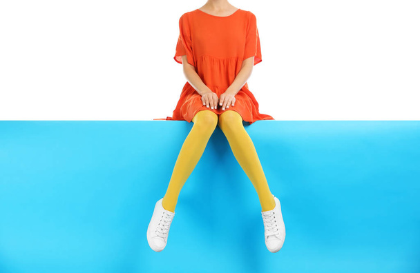 Woman wearing yellow tights and stylish shoes sitting on color b - Zdjęcie, obraz