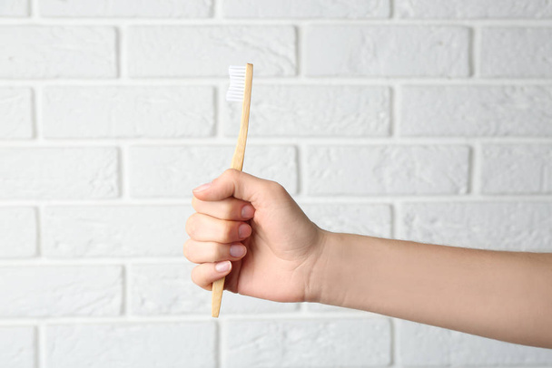 Woman holding bamboo toothbrush against white brick wall, closeup - Photo, image