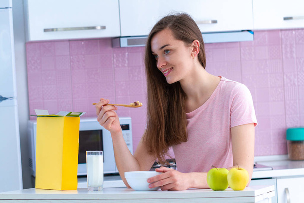 glückliche attraktive Frau isst knusprige Schokoladenbällchen für ein gesundes Müsli-Frühstück, während sie morgens in der heimischen Küche fernsieht  - Foto, Bild