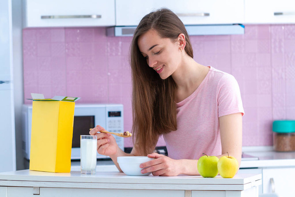 Усміхаючись, щаслива приваблива жінка їсть хрусткі шоколадні кульки для здорових зернових сніданок вранці на кухні вдома
  - Фото, зображення