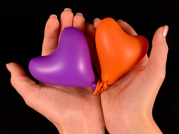 Ballons gonflables lumineux en forme de coeur dans les mains. Deux cœurs dans les paumes féminines, sur fond noir. Fille tient un coeur en caoutchouc
. - Photo, image