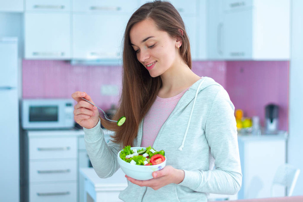 Jovem mulher vegetariana bonita feliz comendo salada de legumes para lanche em casa. Dieta e alimentação fitness. Alimentos limpos e saudáveis
  - Foto, Imagem