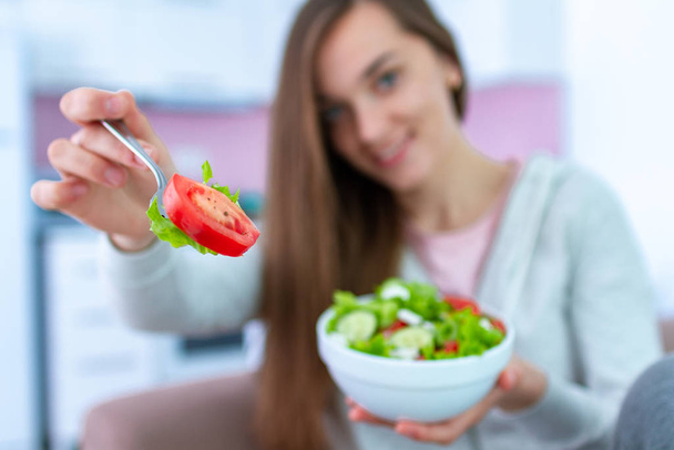 Porträt einer jungen, glücklichen, gesunden Frau, die zu Hause frischen Gemüsesalat isst. ausgewogene Ernährung und Fitness-Ernährung. Saubere und kontrollierte Lebensmittel  - Foto, Bild
