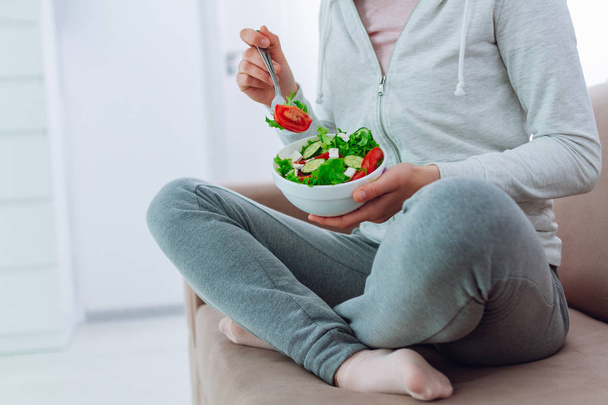 Healthy woman in sportswear holding a bowl of fresh vegetable salad at home. Balanced organic diet and clean fitness eating.  - Fotoğraf, Görsel