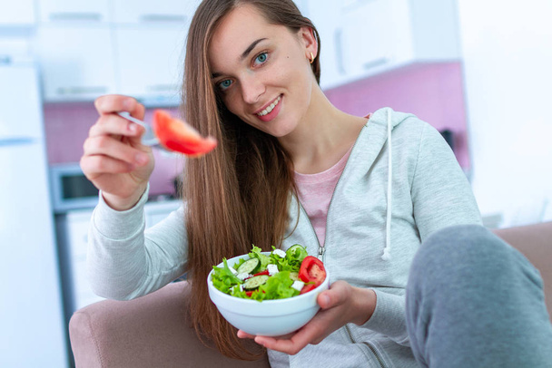 Портрет молодой счастливой здоровой женщины, которая ест овощной салат на обед дома. Диета и фитнес-питание. Чистота и контроль продуктов питания
  - Фото, изображение