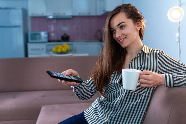 Young happy smiling woman sitting on couch, resting and watching various comedy tv programs on television at home - Фото, зображення