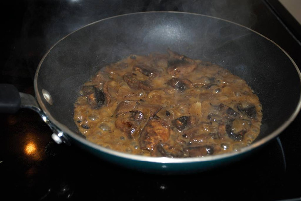 salteando champiñones y cebollas en una sartén con aceite, condimento y vapor
 - Foto, imagen
