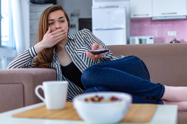Woman resting on the couch and yawning while watching TV alone at home  - Foto, imagen