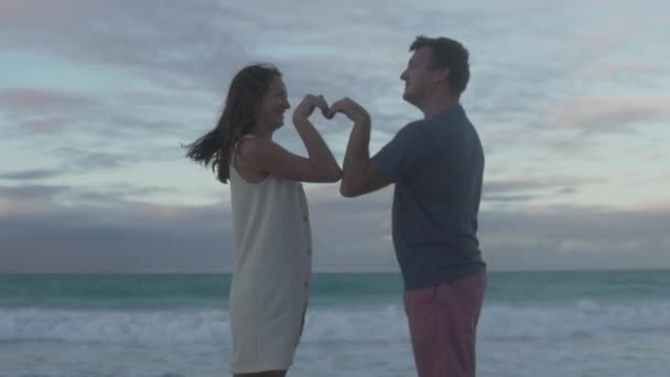 Ein verliebtes Paar macht sich vor dem Hintergrund des Ozeans ein Herz aus der Hand - Filmmaterial, Video