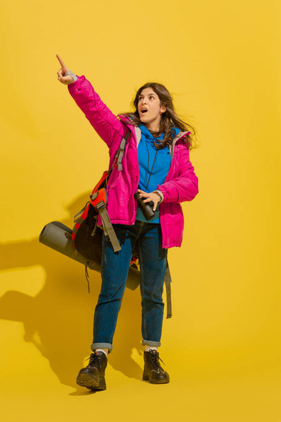 Full length portrait of a cheerful young caucasian tourist girl isolated on yellow background - 写真・画像
