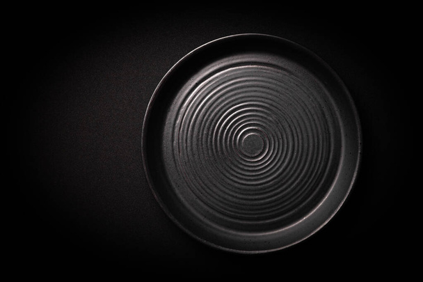 Nahaufnahme leere runde schwarze Keramikteller mit Kreismuster auf dunklem Hintergrund mit Kopierraum. Blick aus der Vogelperspektive. Konzept modernes Schießmenü vom Koch, Restaurantanzeige, Geschirr-Kataloge, Top - Foto, Bild
