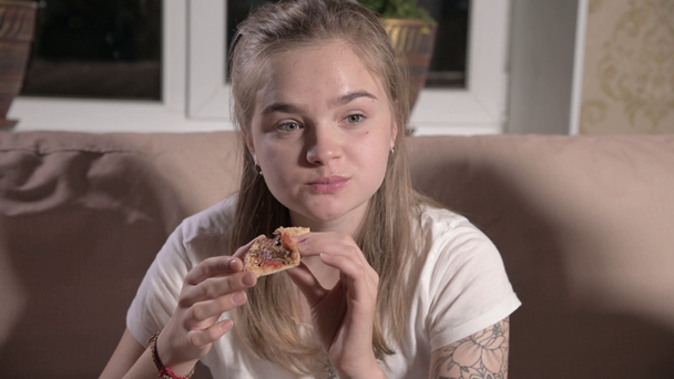 Young cute woman sits in living room on sofa, watches TV, eats pizza. Close-up - Video