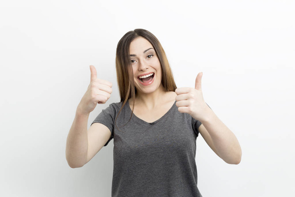 Happy young woman holds thumb up showing great mood. - 写真・画像