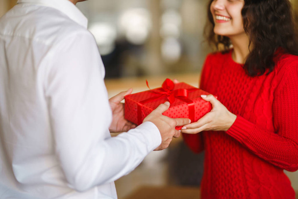 Man gives to his woman a gift box with red ribbon. A loving couple cuddles and celebrating Valentine's Day in the restaurant. Valentine's Day, holiday and surprise concept. Relationship and love. - Zdjęcie, obraz