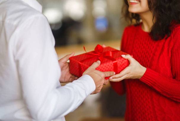Man gives to his woman a gift box with red ribbon. A loving couple cuddles and celebrating Valentine's Day in the restaurant. Valentine's Day, holiday and surprise concept. Relationship and love. - Foto, immagini