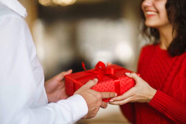 Man gives to his woman a gift box with red ribbon. A loving couple cuddles and celebrating Valentine's Day in the restaurant. Valentine's Day, holiday and surprise concept. Relationship and love. - Fotoğraf, Görsel