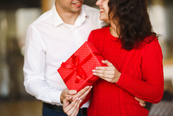 Man gives to his woman a gift box with red ribbon. A loving couple cuddles and celebrating Valentine's Day in the restaurant. Valentine's Day, holiday and surprise concept. Relationship and love. - Foto, Imagem