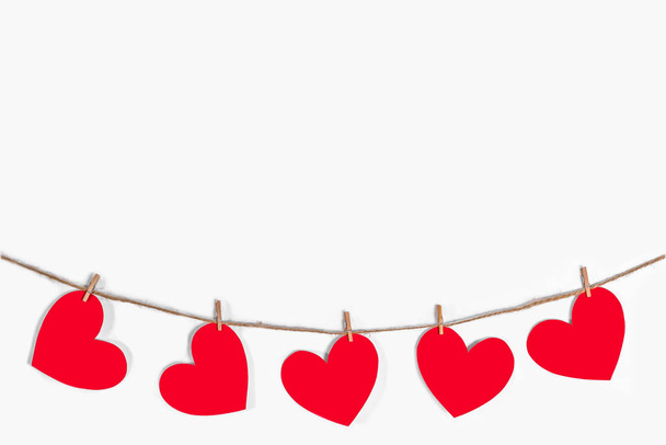 Garland of red hearts on a white isolated background. Natural rope and clothespins. The concept of recognition in love, romantic relationships, Valentines Day. Copy space - Фото, зображення