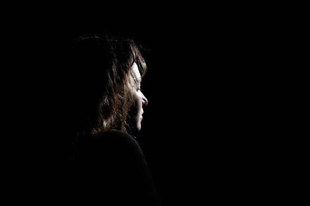 silhueta no perfil de uma menina solitária e triste em um fundo preto
 - Foto, Imagem