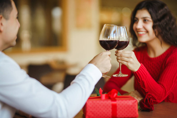 Young couple having a romantic dinner and toasting with glass of red wine. Sweet couple celebrate their anniversary. Valentines day celebration concept. Relationship, surprise and love concept. - Photo, Image