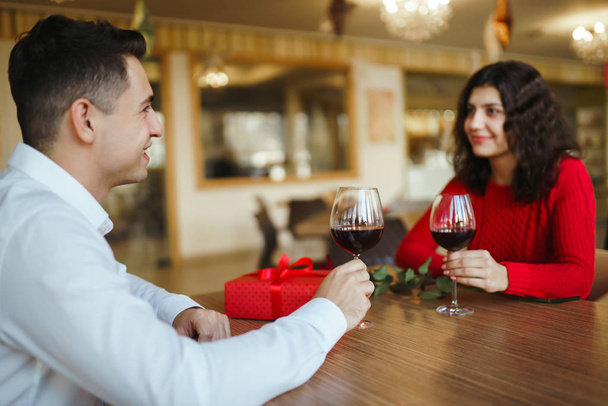 Young couple having a romantic dinner and toasting with cups of red wine. Sweet couple celebrate their anniversary. Valentines day celebration concept. Relationship, surprise and love concept. - Fotoğraf, Görsel