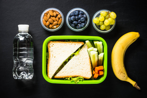 Lunch box with sandwich and fruits on black. - Photo, Image