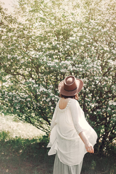 Happy boho woman in hat having fun in sunny light near white blo - Foto, Bild