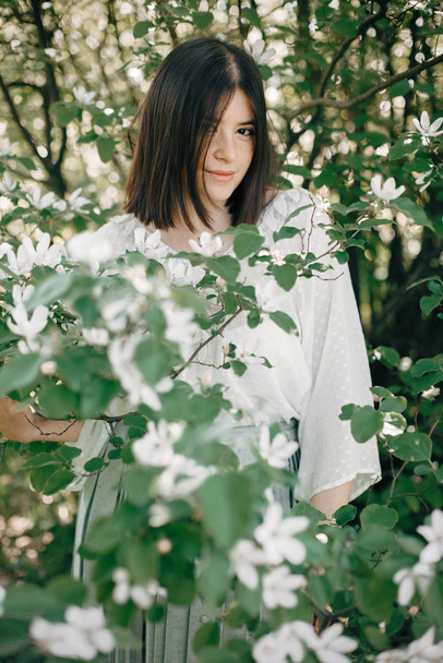 Stylish boho woman posing in white flowers in spring park. Hipst - Photo, Image