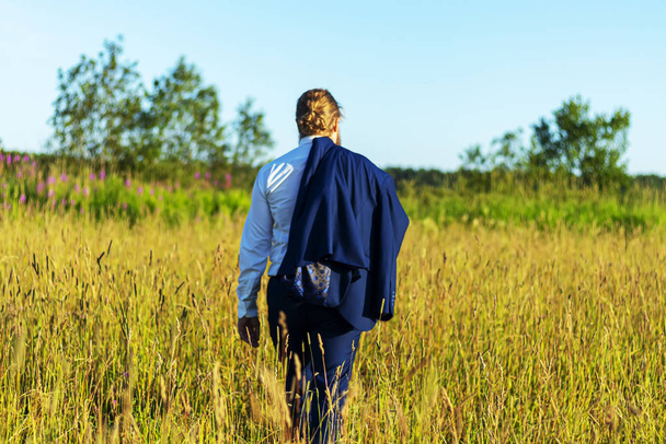 Caucasian man in a suit is walking on the field. Concept businessman in nature - Fotó, kép