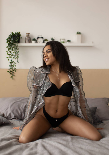 Portrait of a sensual sexy african woman lying on the bed in black lingerie - Zdjęcie, obraz