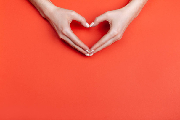 Les mains féminines montrent un symbole de coeur sur un fond rouge. Place pour le texte - Photo, image