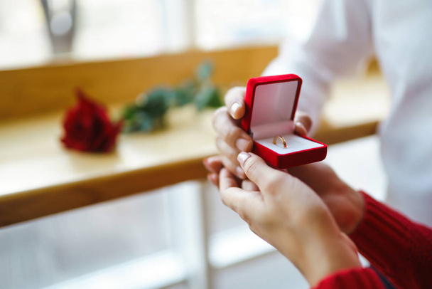 Handsome man proposing a beautiful woman to marry him in restaurant. Surprised attractive woman getting a marriage proposal. Valentines day celebration concept. Relationship and love concept. - 写真・画像