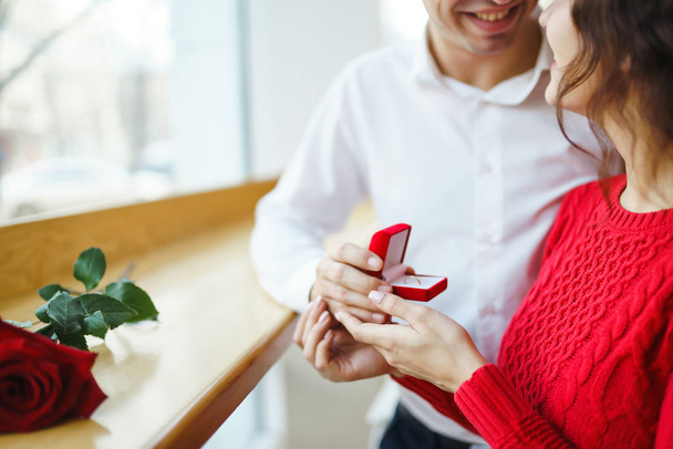 Handsome man proposing a beautiful woman to marry him in restaurant. Surprised attractive woman getting a marriage proposal. Valentines day celebration concept. Relationship and love concept. - Photo, Image