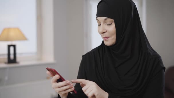 Portrait of excited Muslim woman in traditional clothes scrolling on smartphone and smiling. Cheerful modern eastern lady using social media. Society, lifestyle, eastern culture. - Video