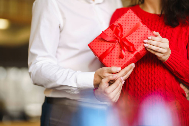 Valentine's Day, holiday and surprise concept. Man gives to his woman a red gift box. Sweet couple celebrate their anniversary. Relationship and love concept. - Photo, Image