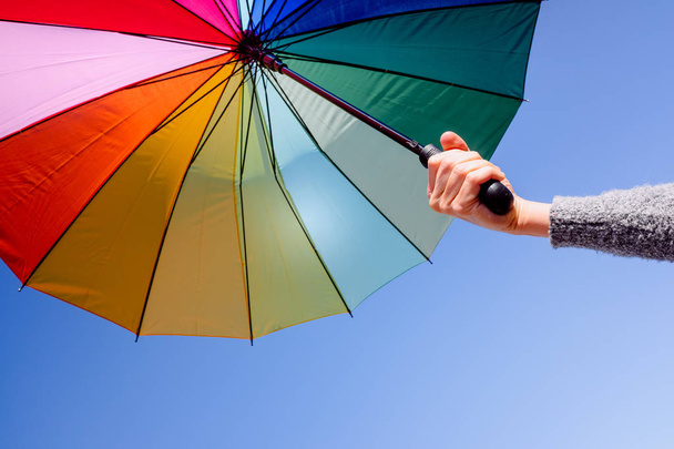 Frau hält an einem Sommertag mit blauem Himmel einen bunten Sonnenschirm in der Hand - Foto, Bild