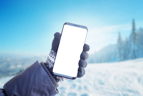 Telefon w dłoni z rękawiczką. Koncepcja korzystania z telefonu komórkowego w zimie, czas zimny. Izolowany ekran do makiety, prezentacja aplikacji - Zdjęcie, obraz