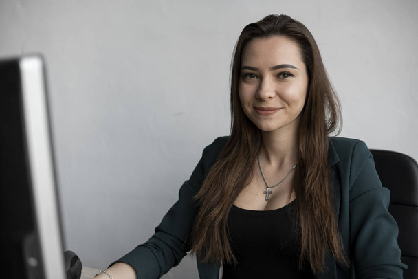 Brunette woman is working in front of a monitor in a office. Business woman working at computer at coworking space. Portrait of happy lady. Female professional working with pc. - Φωτογραφία, εικόνα