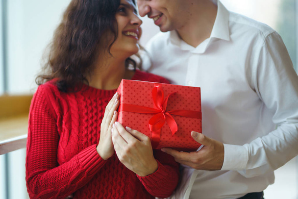 Happy couple with gift hugging. Red gift box in the hands of a couple in love. Valentine's Day, holiday and surprise concept. Lovers give each other presents. Relationship and love concept. - Fotografie, Obrázek