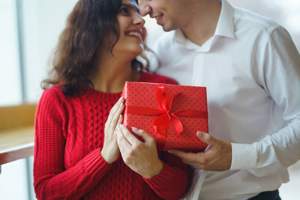 Happy couple with gift hugging. Red gift box in the hands of a couple in love. Valentine's Day, holiday and surprise concept. Lovers give each other presents. Relationship and love concept. - Фото, изображение