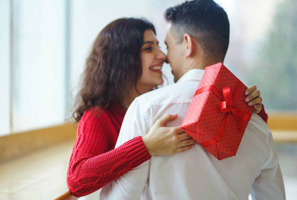 Happy couple with gift hugging. Red gift box in the hands of a couple in love. Valentine's Day, holiday and surprise concept. Lovers give each other presents. Relationship and love concept. - Foto, immagini