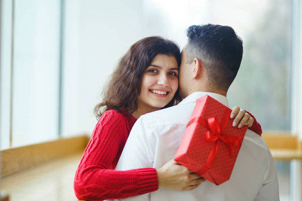 Happy couple with gift hugging. Red gift box in the hands of a couple in love. Valentine's Day, holiday and surprise concept. Lovers give each other presents. Relationship and love concept. - Foto, imagen
