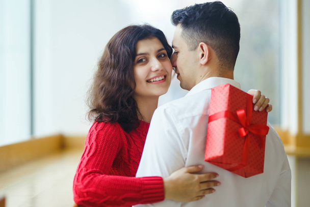 Happy couple with gift hugging. Red gift box in the hands of a couple in love. Valentine's Day, holiday and surprise concept. Lovers give each other presents. Relationship and love concept. - Photo, Image