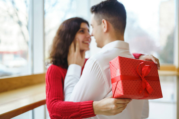 Happy couple with gift hugging. Red gift box in the hands of a couple in love. Valentine's Day, holiday and surprise concept. Lovers give each other presents. Relationship and love concept. - Photo, image